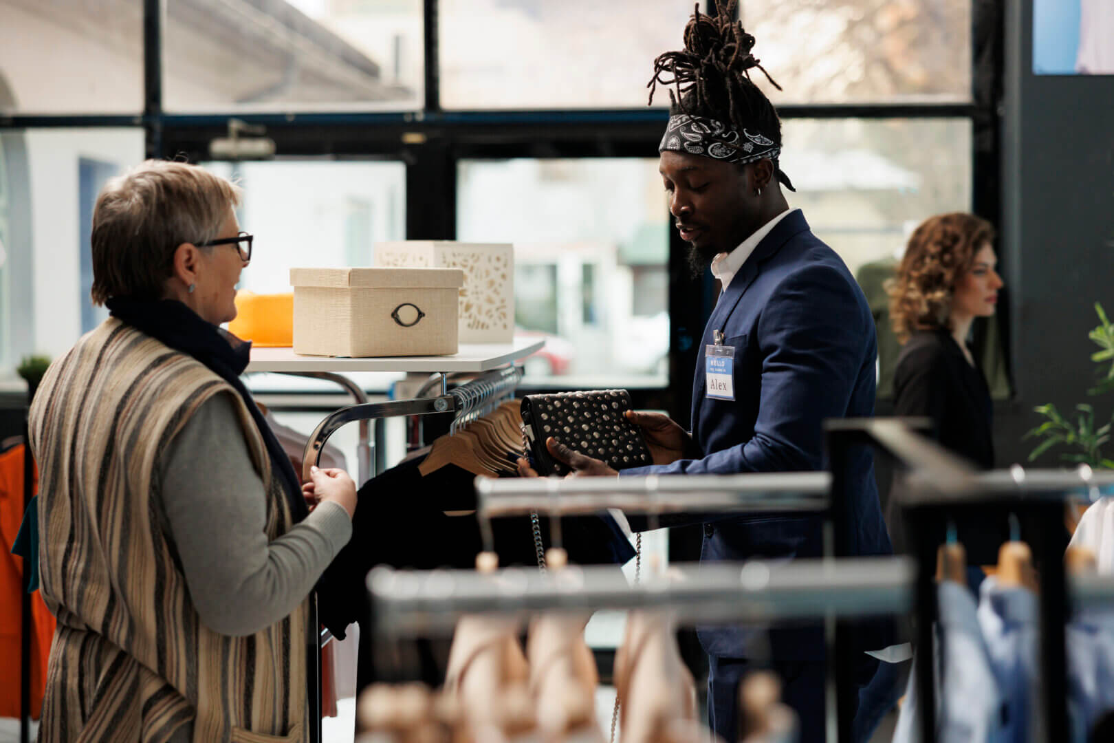Boutique worker helping senior client choosing black bag, shopping for casual wear in modern showroom. Elderly woman buying fashionable merchandise and trendy accessories. Fashion concept