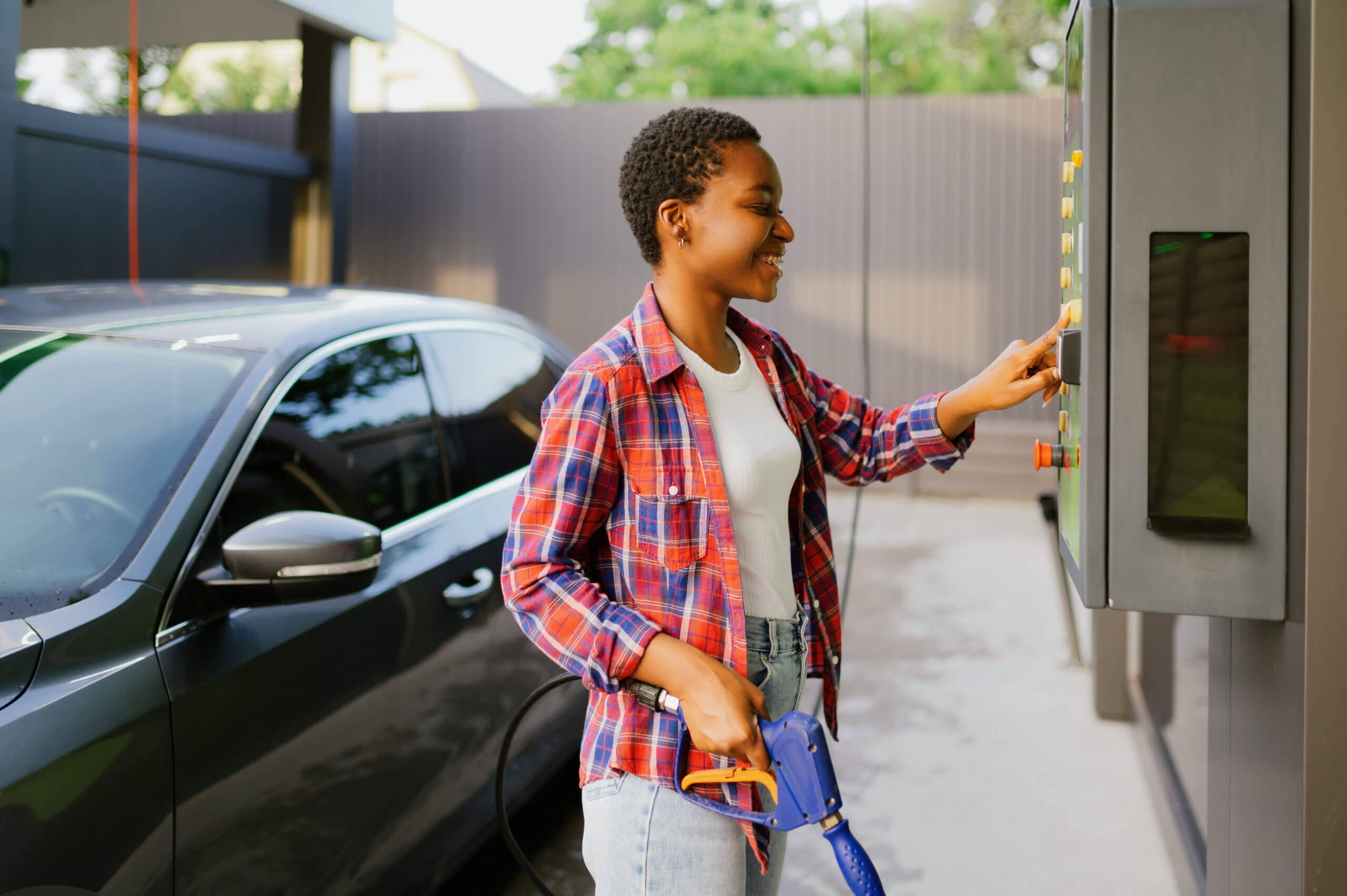 Woman choosing program on water gun, car wash station. Carwash industry or business. Female person cleans her vehicle from dirt outdoors